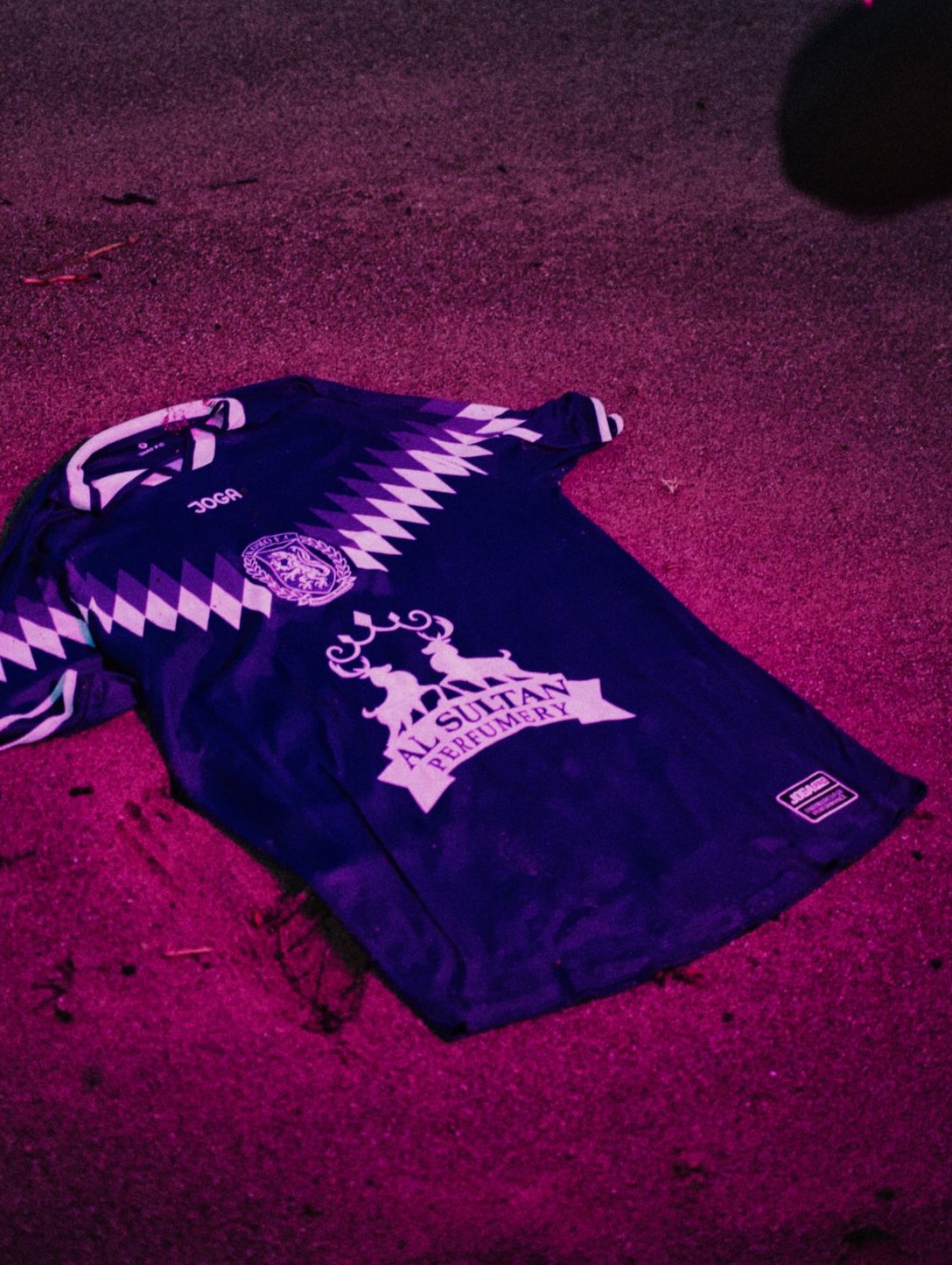 The KOMO F.C. season two home shirt, purple with a lilac zigzag, laid out on the sand
